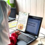 دانش‌آموزی در حال کار با لپ‌تاپ و مطالعه دفتر درسی در کلاس درس