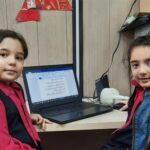 دو دانش‌آموز در حال کار روی لپ‌تاپ در سایت کامپیوتر، یکی از آن‌ها کد فارسی را روی صفحه‌نمایش اصلاح می‌کند