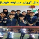 دانش‌آموزان برندۀ مسابقه فوتبال که مدال‌های طلا، نقره و برنز پوشیده‌اند و در زمین سبزِ حیاط مدرسه ایستاده‌اند؛ پایین‌تر دانش‌آموزان دیگری در حال بازی فوتبال