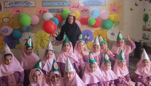 دانش‌آموزانی در حال برگزاری جشن رنگین با کلاه‌های جشنی، لباس‌های صورتی و تزئینات گلوله‌های رنگی در کلاس درس