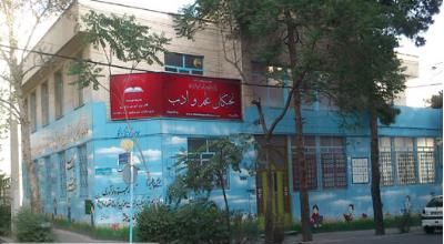 نمای بیرونی ساختمان مدرسه با درب ورودی و تابلوی قرمز و دیوار آبی‌رنگ