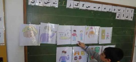 دانش‌آموزی در حال نقاشی و ایجاد اثر هنری روی تخته سیاه کلاس درس، میان دیگر نقاشی‌های دانش‌آموزان