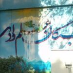 نمای خارجی دیوار آبی ساختمان مدرسه با تابلوی فارسی و درخت در کنار
