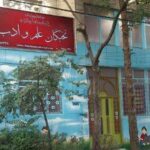 نمای بیرونی ساختمان مدرسه نخبگان المعداب با تابلوی قرمز و دیوارنقاشی شده رنگی