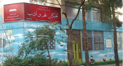 نمای بیرونی ساختمان مدرسه نخبگان المعداب با تابلوی قرمز و دیوارنقاشی شده رنگی