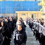 دانش‌آموزان در حال تجمع برای یک مراسم رسمی در حیاط مدرسه با پرچم ملی ایران