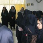 دانش‌آموزان دختر در حال شرکت در یک نشست گروهی یا فعالیت جمعی درون کلاس درس، در حالی که مربی یا معلم نیز حضور دارد