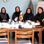 گروهی از معلمان و کودکان در حین شرکت در مراسم ضیافت مدرسه، نشسته‌اند دور میزی با غذا