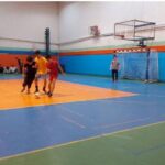 دانش‌آموزان در حال تمرین والیبال در سالن ورزشی مجهز با کفپوش رنگی و شبکه والیبال