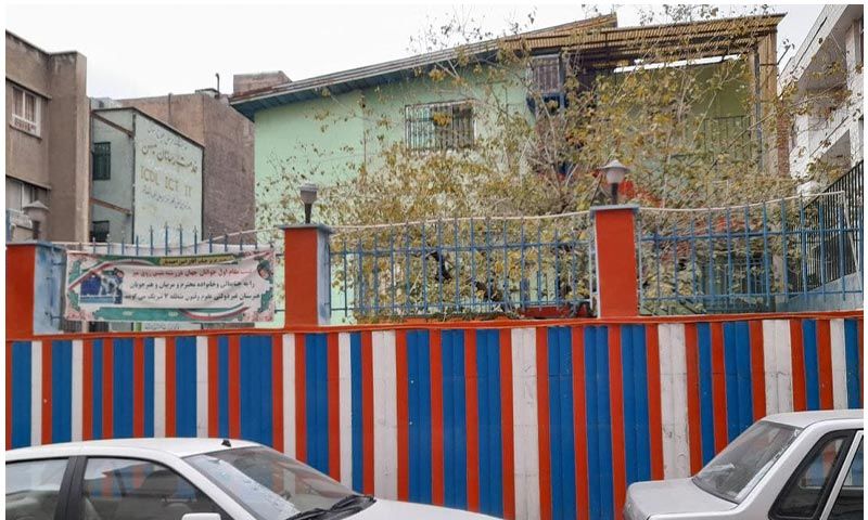 نمای ورودی اصلی مدرسه با تابلو و دروازهٌ رنگی قرمز و آبی