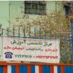 نمای بیرونی درب ورودی ساختمان مدرسه با دیوار سبز و درب فلزی آبی و نارنجی