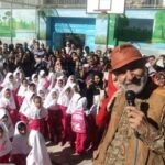 مراسمی درون سالن مدرسه با حضور دانش‌آموزان دختر پوشیده و یک مقام یا میهمان در حال سخنرانی با میکروفون