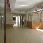 راهرو داخلی پس‌زمینی مدرسه با دیوارهای آجری، روشنایی سقفی، تزئینات موقت قرمز و سبز، و درب‌های کلاس‌درسی