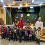 عکس گروهی از دانش‌آموزان و معلمان در حین برگزاری یک مراسم تمثیلی و فرهنگی در سالن اجتماعات مدرسه با لباس‌های شخصیت و تزئینات رنگی