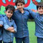 چهار دانش‌آموز با لباس آبی در حیاط مدرسه در حال شرکت در یک فعالیت هنری گروهی کنار تابلوی رنگی