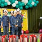 دانش‌آموزان با لباس و کلاه یکسان در حال اجرای مراسمی در سالن، با یک موسیقاردار در پیانو