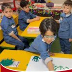 دانش‌آموزان در حال انجام فعالیت هنری و صنایع دستی بر روی میزهای رنگین