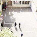 نمایی از بالا از حیاط مدرسه با سطح بتونی و خطوط سفید‌رنگ، برخی دانش‌آموزان در حال تحرک