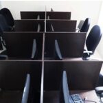 نمای هوایی از سالن کامپیوتر مدرسه با میزهای کار مشکی و صندلی‌های آبی