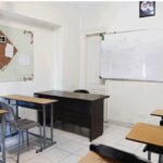 نمای داخلی کلاس درس با میزهای دانش‌آموزی چند نفره، صندلی‌های آبی و سیاه، تخته سفید بزرگ، دکوراسیون دیواری شامل نقاشی قهوه‌ای، تاسیسات تهویه و نورپردازی
