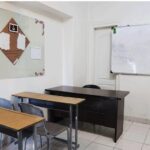 دید داخلی کلاس درس با میز‌های چوبی، صندلی‌های آبی، تخته سفید و دکوراسیون دیوار