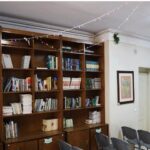 کتابخانه مدرسه با قفسه‌های چوبی پر از کتاب‌های متنوع رنگ‌ها و صندلی‌های سیاه برای مطالعه