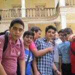 گروهی از دانش‌آموزان ایستاده برای عکس یادگاری جمعی در حیاط مدرسه، ساختمان با معماری سنتی در پس‌زمینه