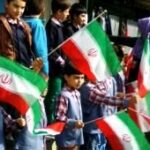 دانش‌آموزان در حیاط مدرسه با پرچم‌های ملی ایران در مراسم ملی