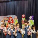 دانش‌آموزانی در لباس فرم مدرسه در حین ایفای نقش در صحنه‌ای تئاتری با تزئینات بادکن‌های رنگی و پوستر در پس‌زمینه