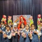 دانش‌آموزان دختر در یونیفورم‌های مدرسه در یک رویداد گروهی با تزیینات بالون‌ی رنگی و پس‌زمینه‌های تزیین‌شده شرکت می‌کنند