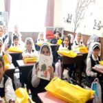 دانش‌آموزان پوشش اسلامی در کلاس درس در حال شرکت در یک فعالیت جمع‌آوری گروهی، بسیاری اشیائی زردِ در دستان دارند و یکی نقاشی نگاه می‌کند