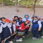 گروهی از دانش‌آموزان با لباس‌های رنگی و نقش‌های مختلف در حیاط مدرسه درحین یک فعالیت نقش‌گری و بازی تعاونی گروهی