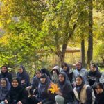 دسته‌ای از دانش‌آموزان دختر با فرم مدرسه در حیاط زیر درختان تنومند به‌هنگام برگزاری مراسم یا فعالیت جمعی