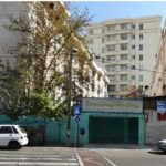 نمای بیرونی ورودی اصلی مدرسه با تابلوی راهنما، درب سبز‌رنگ و خیابان مقابل