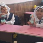 دو دانش‌آموز دختر در حال انجام فعالیت آزمایشی علمی با فلاسک‌های شیشه‌ای رنگی در محیط کلاس درس