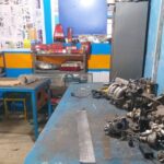 کارگاه تعمیر خودرو و مکانیک مدرسه با میزهای کار، قطعات موتور و تجهیزات آموزشی برای آموزش دانش‌آموزان