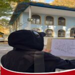 نمای بیرونی ساختمان مدرسه با دیوار آبی سفید، درب‌های شطرنجی و سقف سرمه‌ای