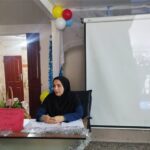 معلمی در حال سخنرانی در یک رویداد مدرسه‌ای با استفاده از پروژکتور، تزیینات بادکنک و پذیرایی