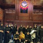 گروهی از دانش‌آموزان در راهروی فاخری مدرسه با سقف و دیوارهای چوبی، تابلو هنری متنوع و دکوراسیون‌های تزئینی