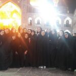 گروهی از دانش‌آموزان دختر مدرسه ایستاده در حیاط بنای تاریخی و مذهبی، در حال عکس یادگاری جمعی با معماری اسلامی و کاشی‌کاری رنگی در پس‌زمینه