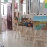 نمایشگاه آثار هنری و نقاشی‌های دانش‌آموزان در راهروی مدرسه، با چندین اثر بر روی سه‌پایه‌های چوبی در کنار سالن‌های کلاس‌درس