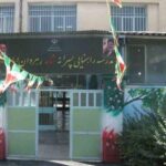 درب ورودی و سردر مدرسه با تابلو نوشته‌شده و پرچم‌های رنگارنگ