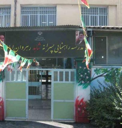 درب ورودی و سردر مدرسه با تابلو نوشته‌شده و پرچم‌های رنگارنگ