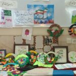 نمایشگاه دیوار داخل مدرسه با آثار هنری رنگی و دست‌ساخت‌های فنری دانش‌آموزان که روی میز و دیوار راهرو نمایش داده شده‌اند