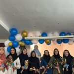 گروهی از معلمان و زنان مدرسه در حال حضور در مراسم تجلیل و تشکر، با تزیینات و گل‌های رسمی