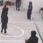 دانش‌آموزان دختر در حال بازی والیبال در حیاط مدرسه با توپ زرد و خطوط سفید کشیده شده روی زمین