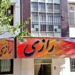 نمای جلوی ساختمان اصلی مدرسه با تابلوی قرمز و درهای سبز، احاطه شده توسط درختان سبز و آسمان ابری
