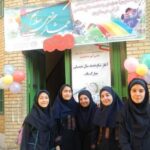 دانش‌آموزان دختر در مراسم آغازین سال تحصیلی پشت درب ورودی مدرسه، میان بادکنک‌های رنگی و بنرهای تزئینی