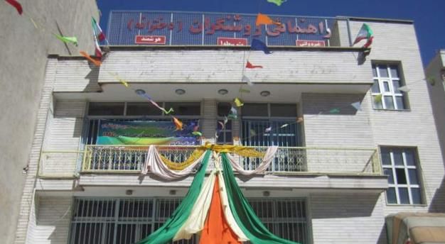 نمای بیرونی ساختمان مدرسه‌ای سفید رنگ با طبقات متعدد، پنجره‌ها، تابلوهای راهنما و دکوراسیون روز ملی