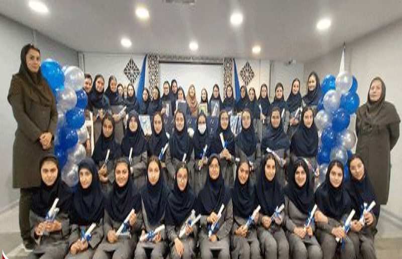 گروهی از دانش‌آموزان دختر و معلمان در مراسم تقدیری مدرسه، حامل کاغذهای سفید (سرتیفیکات یا جوائز) و بالون‌های آبی و سفید برای جشن
